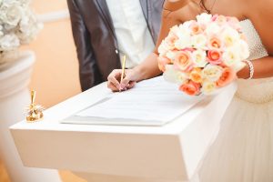 Bride signing a marriage certificate with her bouquet in one hand and a gold pen in another